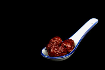 Red Date Jujube on a Ceramic Chinese Soup Spoon isolated on black background. Selective focus.