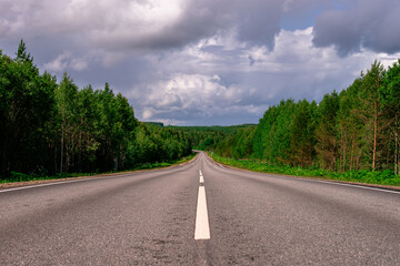 An asphalted intercity road with white markings extending into the distance through a green forest.