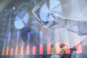 Double exposure of man's hands holding and using a digital device and forex graph drawing. Financial market concept.