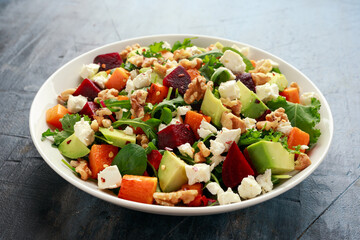 Healthy Butternut squash salad with beetroot, avocado, walnut and feta cheese in white bowl