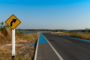 Curved path sign. With blue bike lane on the curved asphalt road. Path around the reservoir of Ang Kep Nam Dok Krai Rayong Thailand.