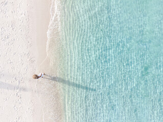 Young woman sitting and relaxing at beautiful tropical white sand beach with wave foam and transparent sea, Summer vacation and Travel background Top view from drone © Kittiphan
