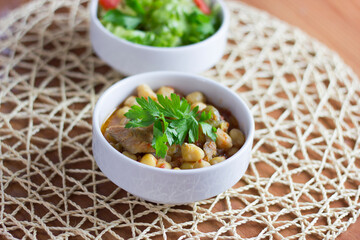 Chickpeas with meat in a white bowl with parsley
