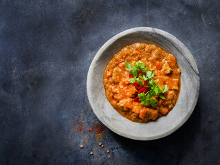 Chicken tikka masala spicy curry meat food in marble plate with spices and parsley on dark textured background with more empty space. Close up, top view. Indian food recipe.
