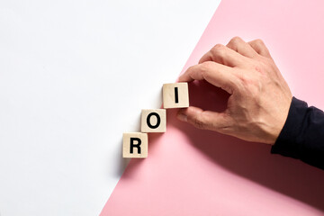 Male hand arranging the wooden cubes with the acronym ROI return on investment. ROI progress,...