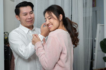 Asian young businessman wearing white long sleeves shirt looking at his wife while helping with buttoning up sleeves and she put her cheek on his hand. Family relationship concept