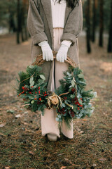 
little girl holding a Christmas wreath of spruce in a pine forest in her hands