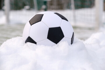 Soccer ball placed on snowdrift near goal in winter on synthetic sports ground
