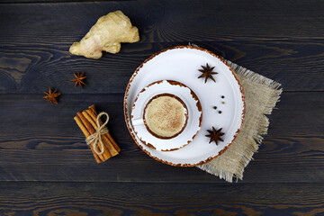 A cup of masala tea on dark wooden background. Traditional Indian tea drink with milk and spices: cinnamon, anise, cardamom, nutmeg, pepper and ginger. Top view.