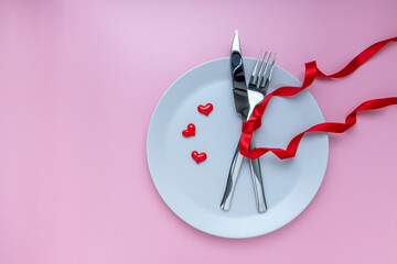 Romantic dinner table. plate, fork and knives with ribbon on pink background. for banner. The concept of Valentine Day. top view, copy space