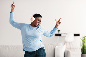 Joyful black woman listening to music in headphones and dancing