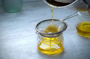The oil is filtered into a glass jar through a metal sieve and cheesecloth. At home.