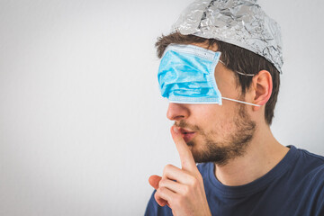 Conspiracy theory concept: Young man with face mask over the eyes and aluminum hat is making a...