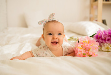 beautiful baby girl lies and smiles with flowers on a bed with a copy of the space