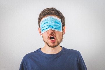 Young angry man is wearing face mask over the eyes and gesturing angry. Conspiracy theory concept.