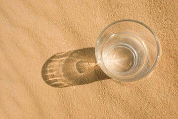 Fototapeta na wymiar Glass of water on sand in desert, top view. Space for text
