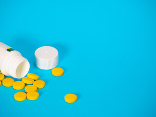 Yellow pills and plastic white bottle. Blue background with copy space for text. Healthy and medicine. Pain management. Drug abuse in teenage concept