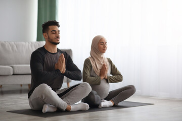 Fototapeta na wymiar Pregnant Muslim Woman In Hijab Meditating Together With Her Husband At Home