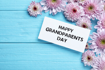 Beautiful flowers and card with phrase Happy Grandparents Day on light blue wooden background, flat...