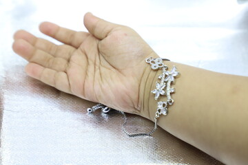 A brown infant baby hand wearing a silver bracelet over shiny silver background with space to write your text