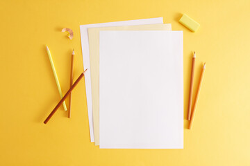Colorful pencils, eraser and empty white papers . Empty place for text or drawing on the yellow...