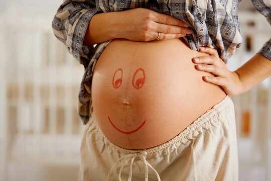 Close-up of pregnant belly with drawn smiley face.