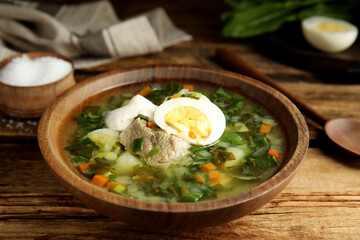Delicious sorrel soup with meat and egg served on  wooden table, closeup