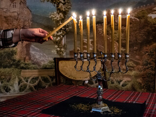 Hand holding a lit candle, lights eight candles on Hanukkah holiday