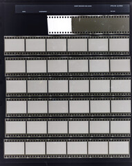 seven long 35mm black and white film strips on dark background behind protection foil with empty frames. 