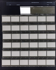 seven long 35mm black and white film strips on dark background behind protection foil with empty...