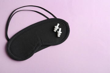 Pair of ear plugs and black sleeping mask on violet background, top view. Space for text