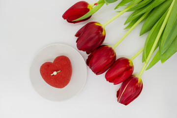 A bouquet of red tulips next to a plate with a heart-shaped cake, in which a gold ring with a diamond
