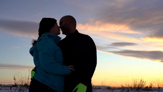 Lovely interracial couple kissing silhouettes with sunset in the background of snowy day