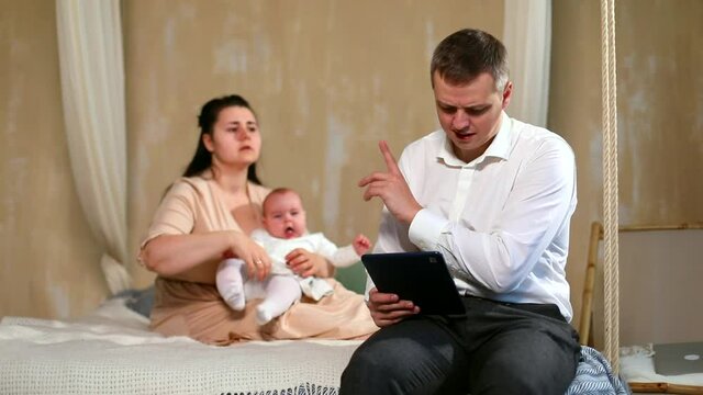 Young busy father working online using laptop talking with angry wife holding baby girl on background. Family healthcare concept. Freelance businessman. Internet addiction. Technology vs humanity.