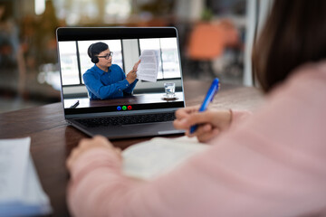 A young teacher wears eyeglasses, headphones explaining lessons to the students via video streaming on the laptop. A young teacher gives an online educational class lecture, consulting to the students