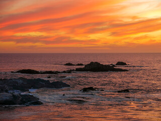 Sunset over Pacific Ocean near Carmel, California with reddish sky. Waves are hitting the rocks in the middle of the sea.