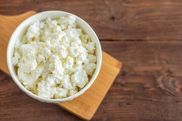 Homemade cottage cheese in a white bowl on a wooden background.