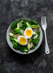 Fototapeta na wymiar Kale, avocado, radish, cucumbers, olive oil salad and soft boiled egg - delicious healthy breakfast, snack on a dark background, top view