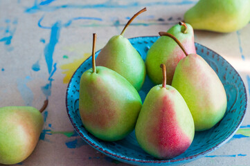 Green pears with red sides lying on a turquoise plate on the table in watercolor paint.