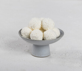 Candies balls of cottage cheese with almonds and coconut chips in a vase on a white background