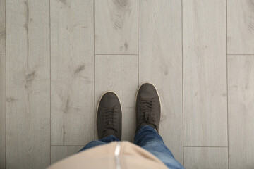 Person in brown shoes standing on wooden floor, top view. Space for text - Powered by Adobe