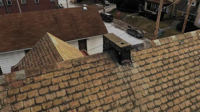 A slow aerial view looking down at a house's slate roof and chimney. Pittsburgh suburbs.  	