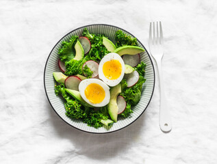 Kale, avocado, radish, cucumbers, olive oil salad and soft boiled egg - delicious healthy breakfast, snack on a light background, top view