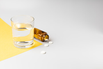 Glass of water and pills from a jar on white and yellow backgrounds