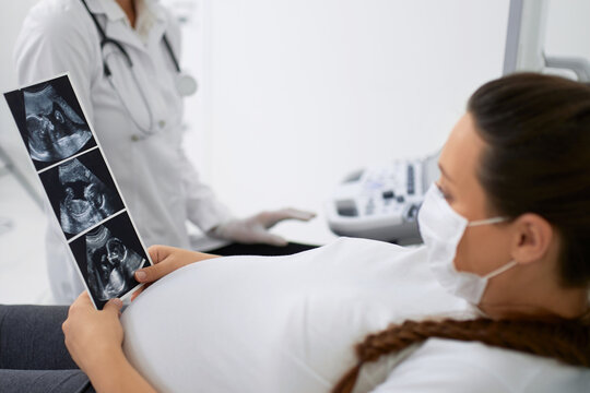 Pregnant woman in mask holding images after ultrasound