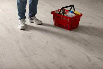 Woman and shopping basket with groceries on wooden floor, closeup. Space for text