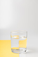 Glass with water on gray and yellow backgrounds