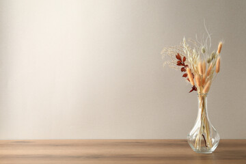 Dried flowers in vase on table against light background. Space for text