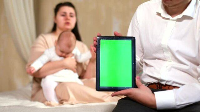 Young father showing green screen tablet closeup. Little baby girl playing with mom on blur background. Chromakey concept. Mock-up. Family application. Children education system. Internet communicate.