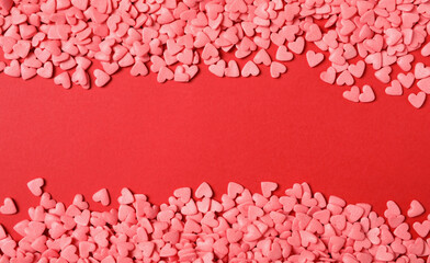 Bright heart shaped sprinkles on red background, flat lay. Space for text